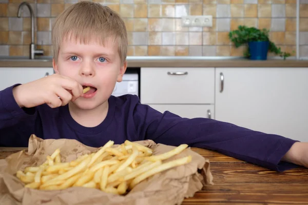 Lindo niño disfrutando de papas fritas en la cocina — Foto de Stock