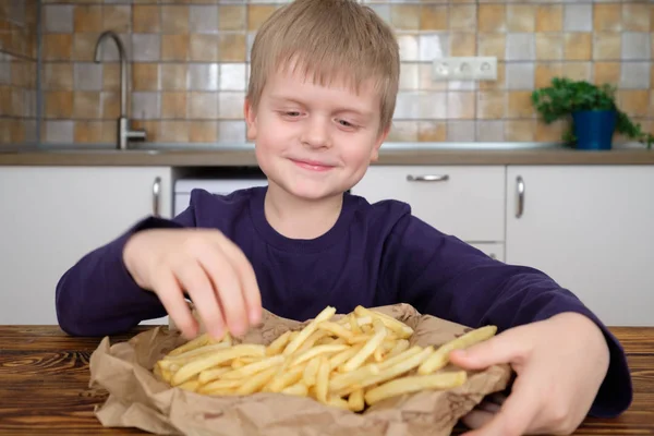 Lindo niño disfrutando de papas fritas en la cocina —  Fotos de Stock