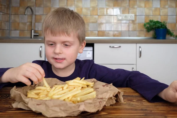 Cute little boy enjoying french fries on kitchen