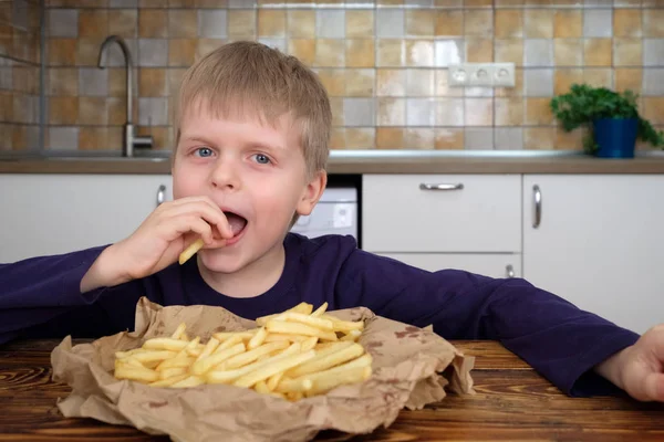 Cute little boy enjoying french fries on kitchen