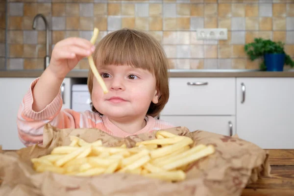 Linda niña disfrutando de papas fritas en la cocina — Foto de Stock