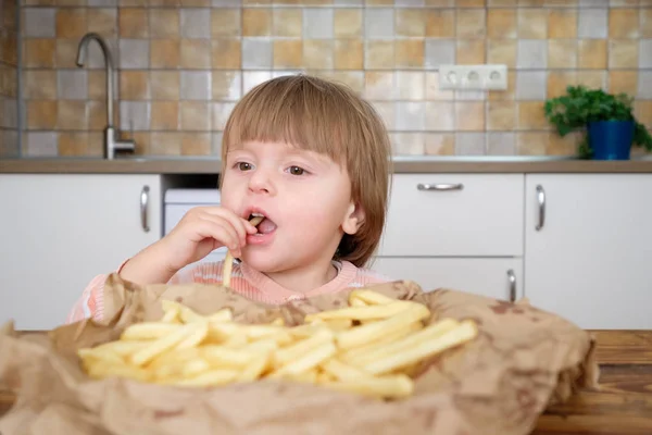 Linda niña disfrutando de papas fritas en la cocina —  Fotos de Stock