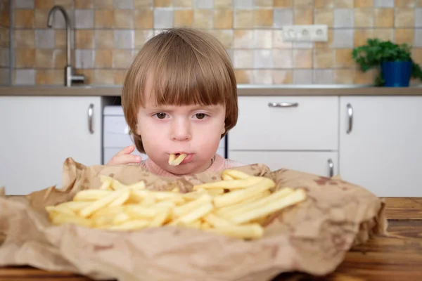 Linda niña disfrutando de papas fritas en la cocina — Foto de Stock