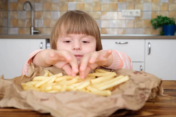 Linda niña disfrutando de papas fritas en la cocina —  Fotos de Stock