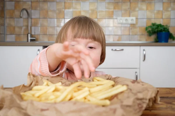 Linda niña disfrutando de papas fritas en la cocina —  Fotos de Stock