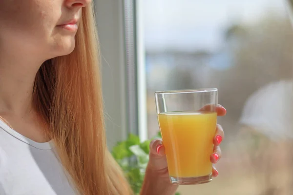 Young blonde woman drinking orange juice and looking at the window — Stock Photo, Image