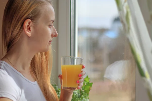 Young beautiful woman drinking juice near window — Stock Photo, Image