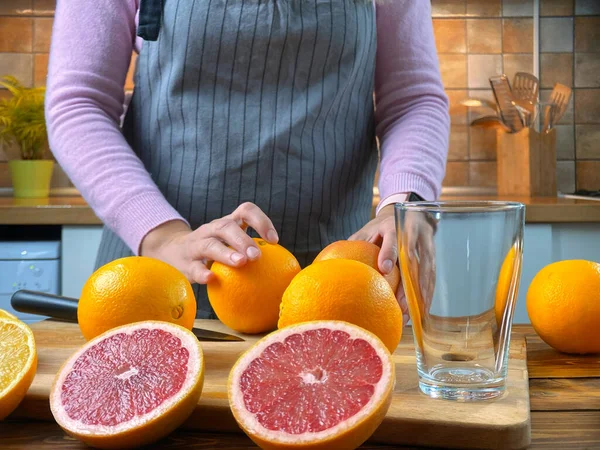 Kvinnan i köket klämmer citrusjuice med en elektrisk juiceapparat. — Stockfoto