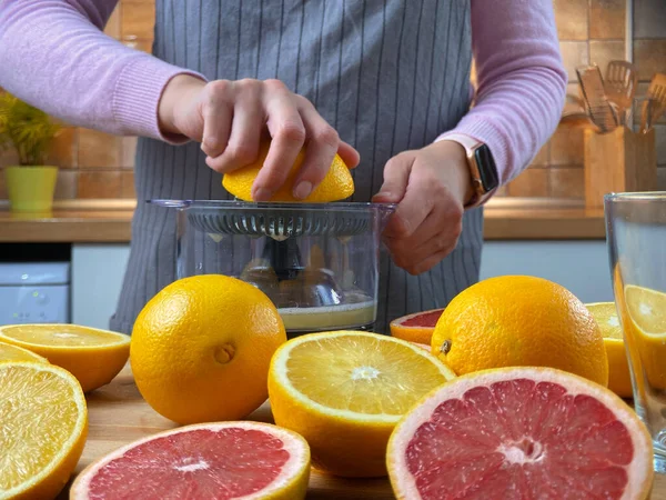 Kvinnan i köket klämmer citrusjuice med en elektrisk juiceapparat. — Stockfoto