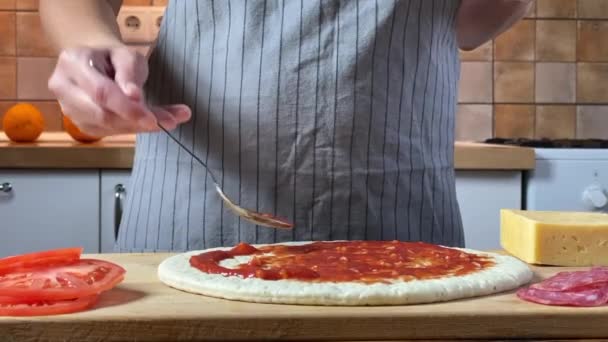 La mujer le pone salsa a la masa. Haciendo pizza italiana en la cocina — Vídeos de Stock