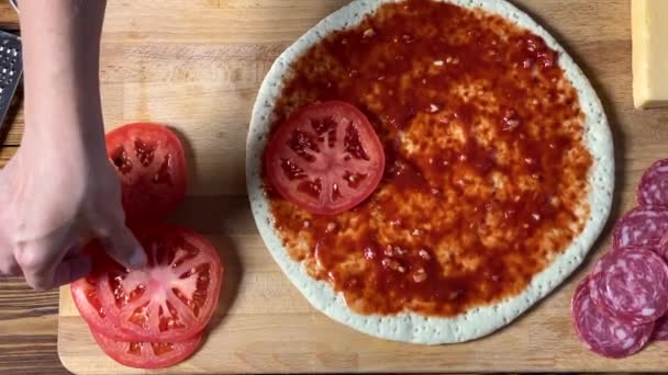 Cozinhar pizza. Mão mulher cozinheiro coloca fatia de tomate na massa . — Vídeo de Stock