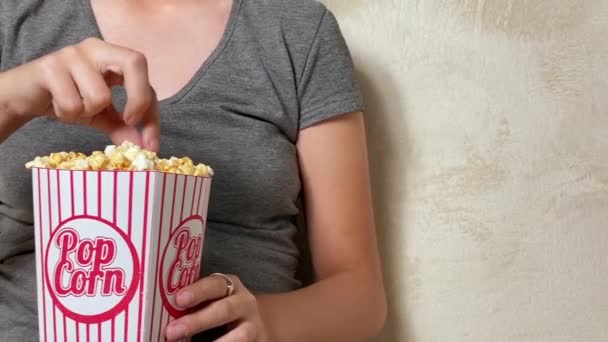 Chica viendo la televisión y comer palomitas de maíz sentado en el sofá en casa — Vídeo de stock