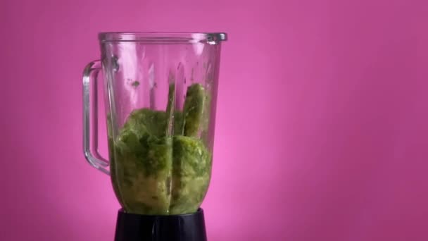 Gezonde groene smoothie gemengd met een blender op roze achtergrond — Stockvideo