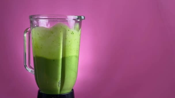 Gezonde groene smoothie gemengd met een blender op roze achtergrond — Stockvideo