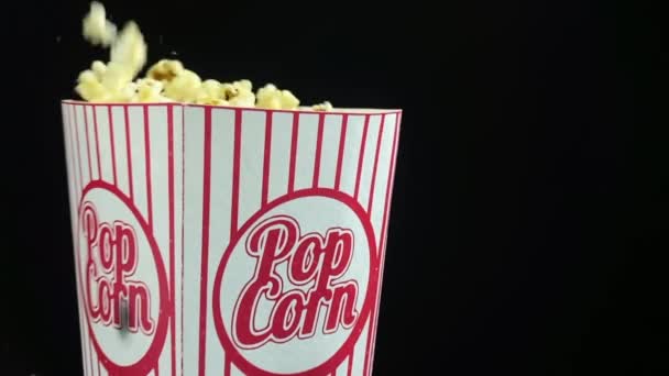 Popcorn πέφτει κάτω σε χαρτόκουτο σε μαύρο φόντο, αργή κίνηση βίντεο — Αρχείο Βίντεο