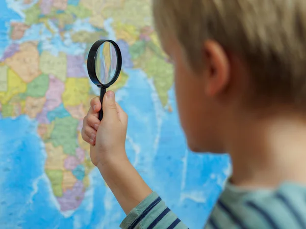 The boy looks at the map through a magnifying glass