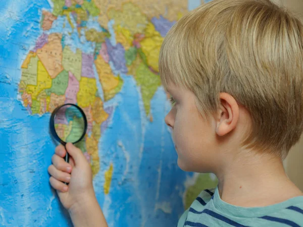 The boy looks at the map through a magnifying glass