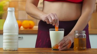 Sportif kız bir bardak badem sütüne bal koyar, ağır çekimde.