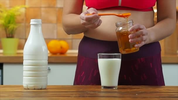 Спортивная девушка кладет мед в стакан миндального молока, замедленная съемка — стоковое видео