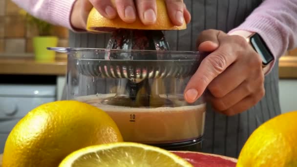 Mujer en la cocina exprimiendo jugo de cítricos con un exprimidor eléctrico . — Vídeo de stock