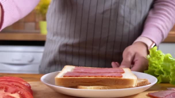 Vrouw koken sandwich op de keuken met salade, spek en tomaat — Stockvideo