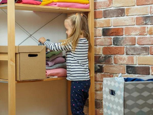 Dziewczynka owija ubrania w kartonowe pudełko w domu — Zdjęcie stockowe