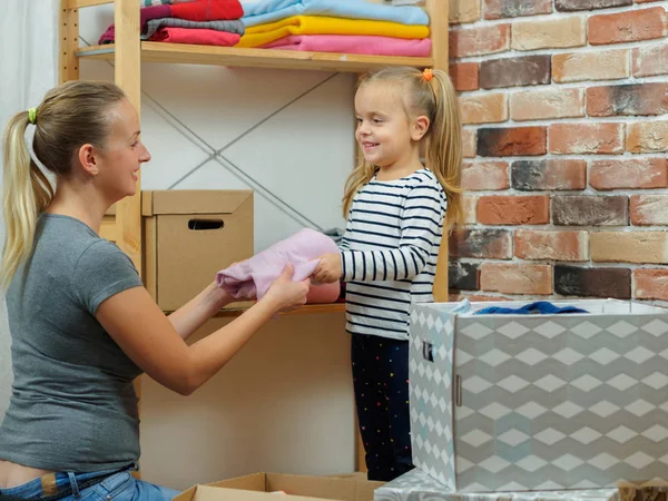 Mutter und kleine Tochter legen unterschiedliche Kleidungsstücke in Kartons — Stockfoto