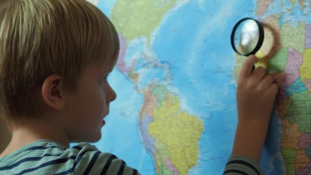 De jongen kijkt door een vergrootglas naar de kaart — Stockvideo