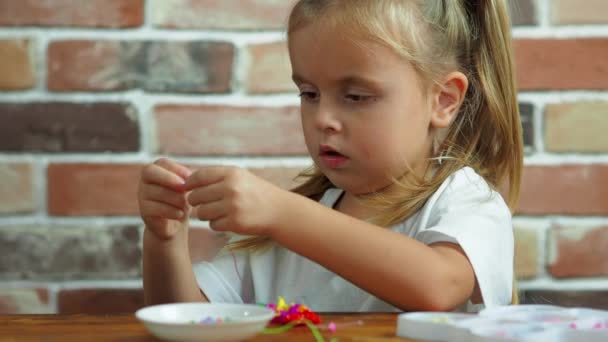 Söt liten flicka gör ett armband av pärlor — Stockvideo