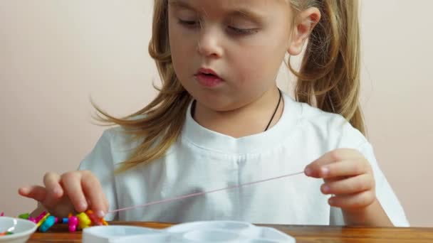 Cute little baby girl make a bracelet from beads — ストック動画