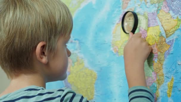 Le garçon regarde la carte à travers une loupe — Video