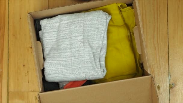 Девушка кладет одежду со стойки в картонную коробку, закрывается — стоковое видео