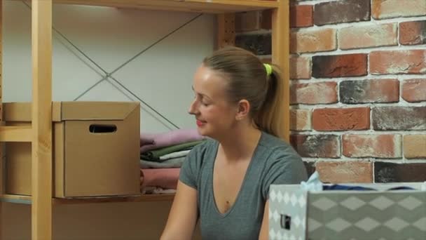 Девушка кладет одежду из стойки в картонную коробку, медленное видео — стоковое видео