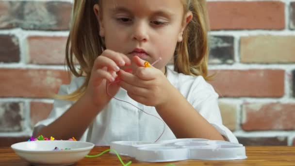Schattig klein meisje maken een armband van kralen — Stockvideo