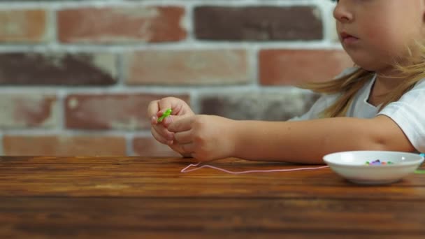 Милая маленькая девочка, сделай браслет из бусин. — стоковое видео