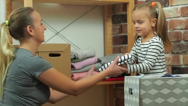 Mom and little daughter put different clothes in boxes, slow motion — ストック動画