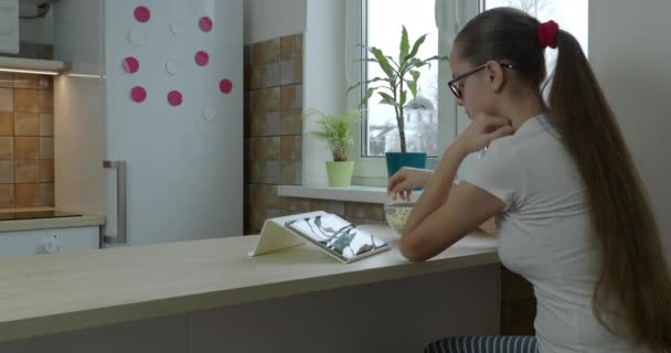 Девочка-подросток смотрит сериал на планшете и ест попкорн — стоковое видео