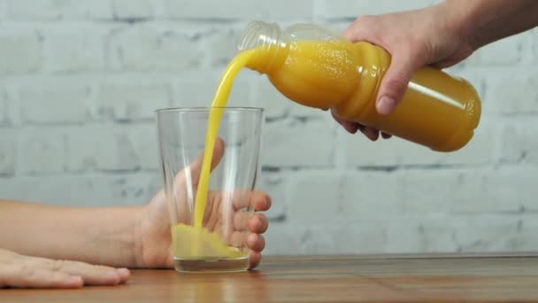 Moeder gieten sinaasappelsap naar glas in de handen van de jongen, slow motion — Stockvideo