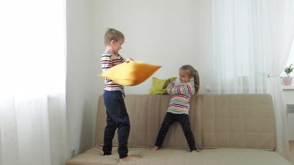 Bruder und kleine Schwester kämpfen mit Kissen auf dem Sofa, Zeitlupe — Stockvideo