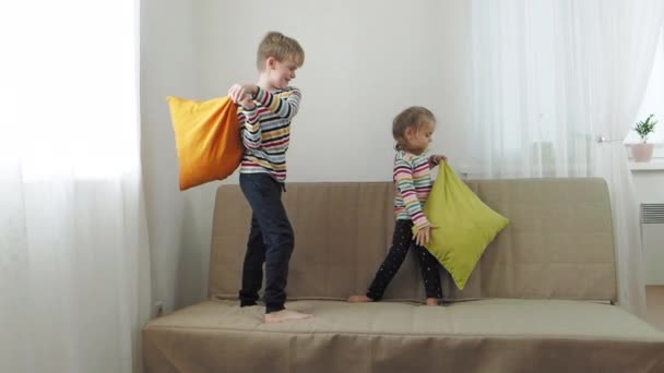 Bruder und kleine Schwester kämpfen mit Kissen auf dem Sofa, Zeitlupe — Stockvideo