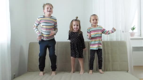 Two baby sister and brother laughing and jumping on sofa, slow motion — Stock Video