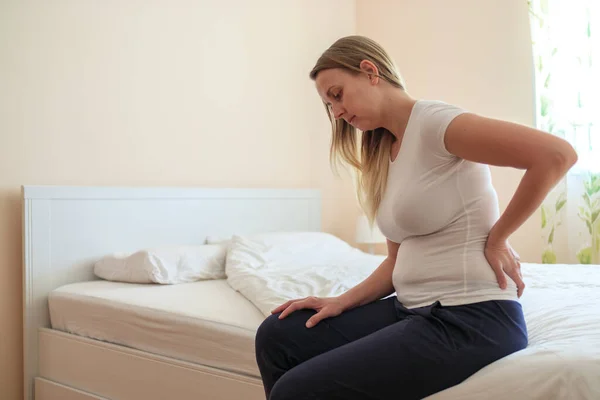 Young plump woman sitting in bedroom with backache