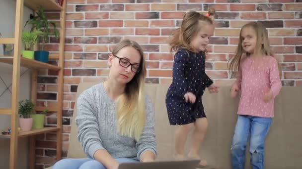 Dos niñas saltando en el sofá y no permitiendo que la madre trabajadora en casa — Vídeo de stock