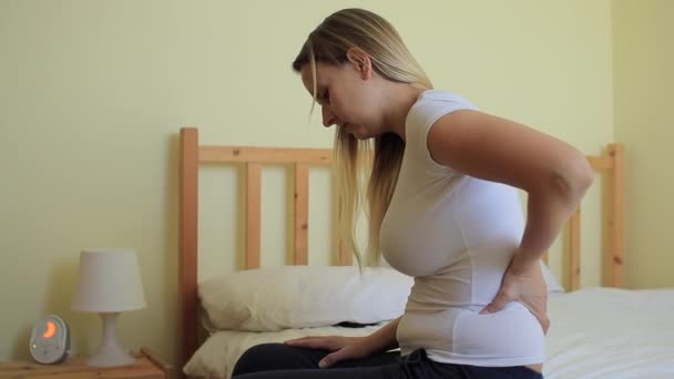 Молодая пухлая женщина сидит в спальне с болью в спине — стоковое видео