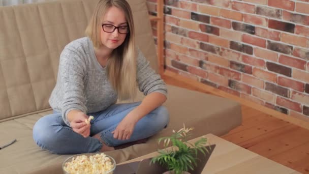 Kobieta siedzi na kanapie w salonie i ogląda seriale z popcornem — Wideo stockowe