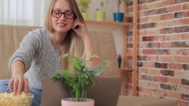 Frau sitzt auf Sofa im Wohnzimmer und schaut Serien mit Popcorn — Stockvideo