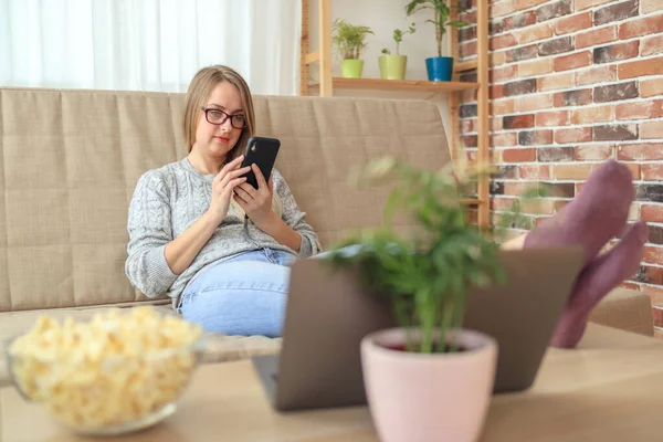 Mladá žena sedí na pohovce v obývacím pokoji a nakupovat smartphone — Stock fotografie