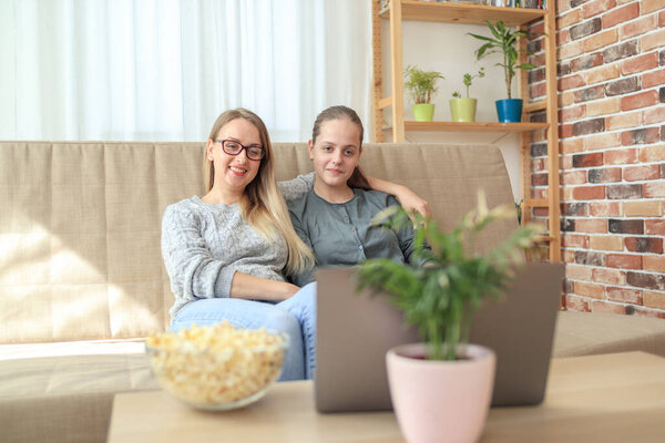 Mother and daughter sitting on sofa in living room together and looking learning course