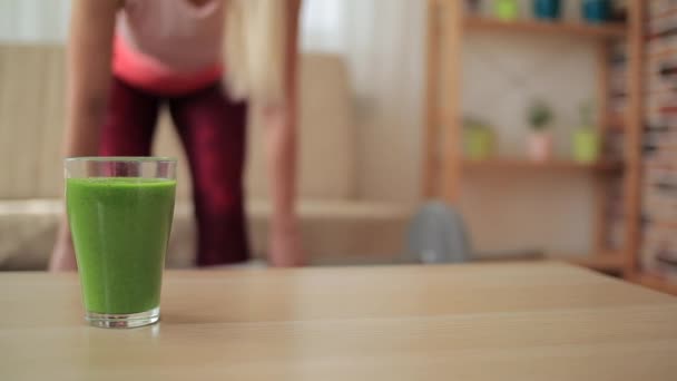 Ένα ποτήρι πράσινο smoothie με θολή γυναίκα που προσπαθεί να χάσει βάρος στο παρασκήνιο — Αρχείο Βίντεο