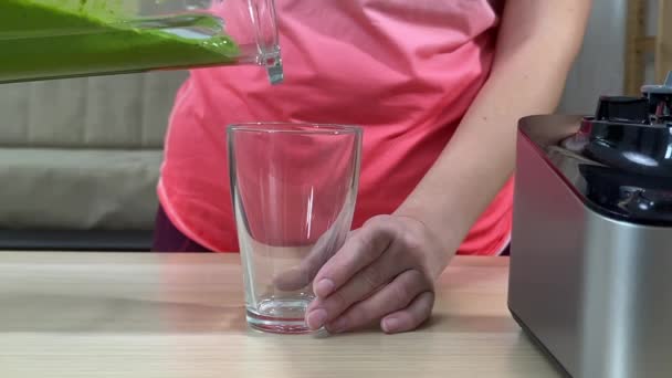 Frau gießt frischen grünen Smoothie aus dem Mixer ins Glas — Stockvideo